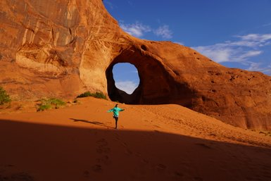 Ein Kind in einem blauen Pullover läuft fröhlich durch die rote Sandlandschaft von Monument Valley, umgeben von beeindruckenden Felsen.