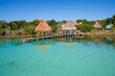 Ein ruhiger Wasserblick auf eine Holzplattform mit einem Strohdach, umgeben von klarem, türkisfarbenem Wasser und üppiger Vegetation.