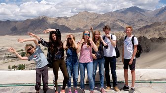 Eine Gruppe von Teenagern posiert fröhlich vor einer beeindruckenden Berglandschaft mit Wolken am Himmel.
