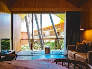 Ein modernes Wohnzimmer mit großen Fenstern, die auf eine grüne Umgebung und Holzarchitektur blicken.