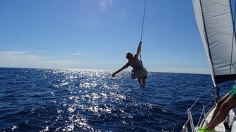 Eine Person in einem gestreiften Kleid schwingt fröhlich über dem glitzernden Wasser des Ozeans, während die Sonne scheint.