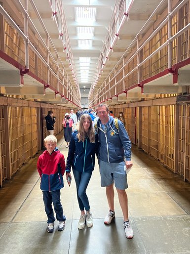 Eine Familie steht in einem historischen Gefängnis mit langen Zellenreihen, die Wände sind aus Stein und Metall.