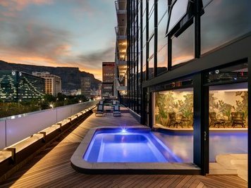 Ein eleganter Balkon mit einem kleinen Pool, umgeben von modernen Gebäuden und einer atemberaubenden Abendkulisse.