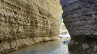 Ein schmaler Canyon mit hohen, geschichteten Felswänden, die von einem ruhigen, trüben Fluss durchzogen werden.