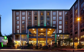 Das Holiday Inn & Suites in Vancouver zeigt eine moderne Fassade mit beleuchtetem Eingangsbereich und grünen Akzenten.