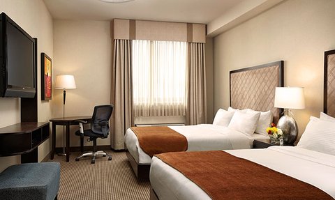 Ein modernes Hotelzimmer mit zwei Betten, einem Schreibtisch und einem Fernseher, das hell und einladend wirkt.