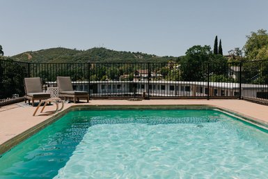 Ein klarer Pool mit grünem Wasser, umgeben von einem schwarzen Zaun und zwei Liegen, bietet einen Blick auf die Hügel.