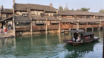 Ein traditionelles Holzboot fährt auf einem ruhigen Wasserweg, umgeben von historischen Gebäuden mit Holzverkleidung.