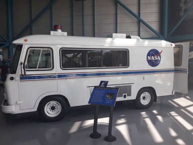 Ein weißer NASA-Astronautenbus steht in einem modernen Ausstellungsraum, umgeben von blauen Stahlträgern.