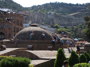 Eine Gruppe von Menschen erkundet die historischen Schwefelbäder in Tiflis, während andere auf den Kuppeln spielen.