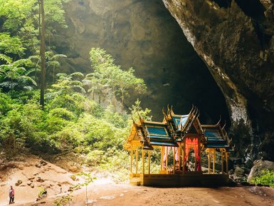 Sonnenstrahlen fallen durch die Öffnung der Phraya Nakhon Höhle auf die umliegenden Bäume - Thailand Familienreise