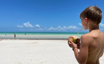 Kind trinkt frisches Kokosnusswasser am Strand von Puerto Morelos – Mexiko Familienreise