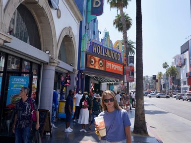 Eine junge Frau steht auf dem Hollywood Boulevard, hält ein großes Getränk und trägt eine modische Sonnenbrille.