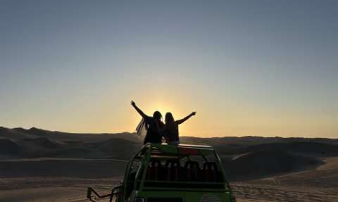 Zwei Frauen stehen auf einem Geländewagen und genießen den Sonnenuntergang über den Sanddünen in Huacachina.