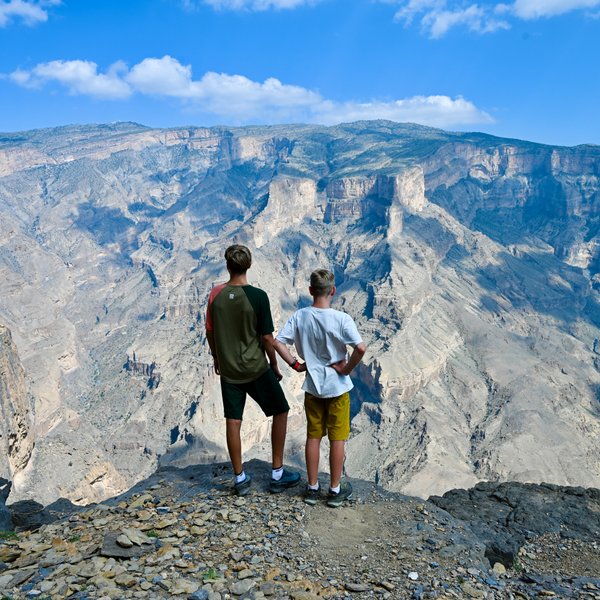 Teenager und Kind blicken gemeinsam auf die atemberaubende Schluchtlandschaft des Jebel Shams – Oman mit Kindern