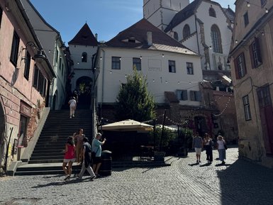 Eine belebte Straße in Sibiu mit einer beeindruckenden Kirche im Hintergrund und Menschen, die die Treppen hinaufgehen.