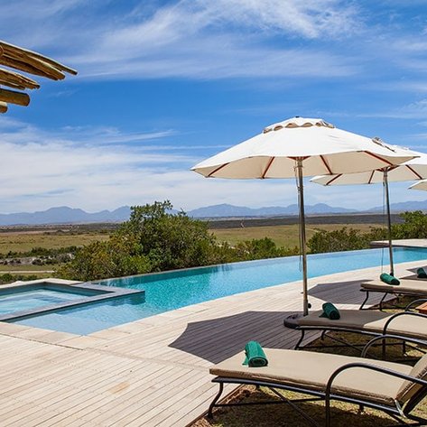 Ein einladender Pool mit Liegen und Sonnenschirmen, umgeben von einer malerischen Landschaft und Bergen im Hintergrund.