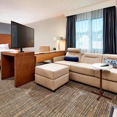 Ein modernes Hotelzimmer mit einem großen Bett, einem Fernseher und einem gemütlichen Sitzbereich mit einem kleinen Tisch.