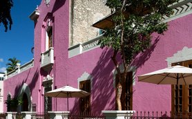 Eine lebhafte, pinkfarbene Fassade eines Gebäudes mit großen Fenstern und Sonnenschirmen im Freien.