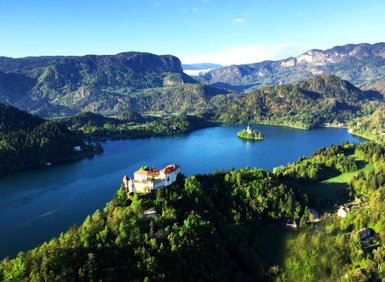 Ein atemberaubender Blick auf den Bleder See, umgeben von üppigen Wäldern und majestätischen Bergen im Hintergrund.