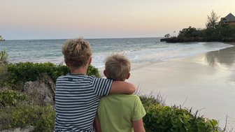 Zwei Jungen stehen am Strand, umarmt, während sie den Sonnenuntergang über dem Meer beobachten.