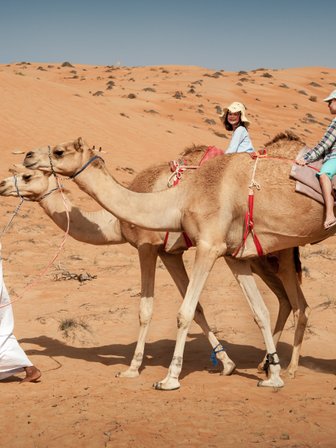 Beduine führt zwei Kamele mit zwei Mädchen durch die Wüste – Oman Familienreise