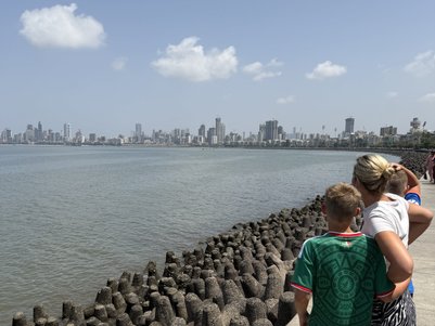Ein Junge und eine Frau stehen am Ufer, blicken auf die Skyline von Mumbai und genießen den sonnigen Tag am Wasser.