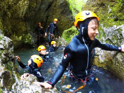 Eine Gruppe von Abenteurern in Neoprenanzügen erkundet einen schmalen, moosbedeckten Canyon mit klarem Wasser.