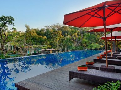 Ein luxuriöser Pool mit reflektierendem Wasser, umgeben von üppigem Grün und Sonnenschirmen in einem tropischen Resort.