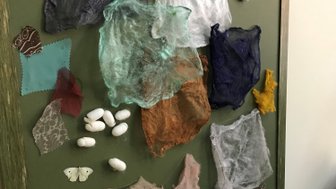 Eine kreative Wandinstallation zeigt verschiedene farbige Stoffe und Kokons, die harmonisch angeordnet sind.