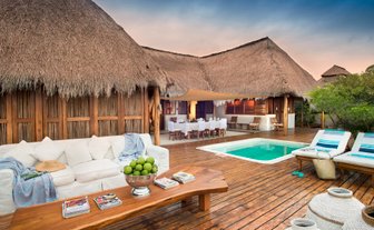 Eine stilvolle Terrasse mit einem Pool, umgeben von einem strohgedeckten Haus und gemütlichen Sitzgelegenheiten aus Holz.