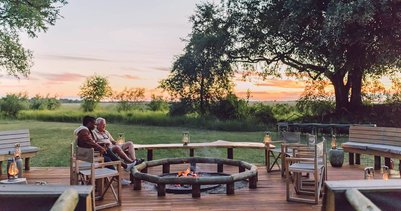 Ein Paar sitzt entspannt am Lagerfeuer, umgeben von einer malerischen Landschaft bei Sonnenuntergang.
