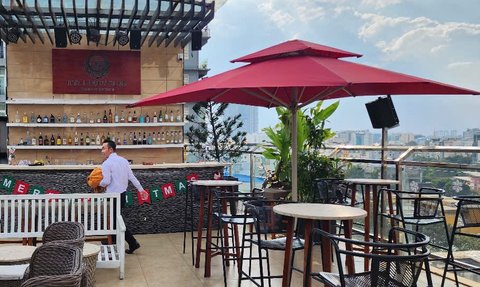 Eine stilvolle Dachterrasse mit einer Bar, umgeben von Pflanzen und einem Blick auf die Stadt, während ein Kellner vorbeigeht.