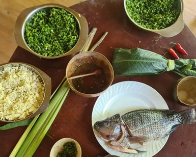 Auf einem Holztisch liegen frischer Fisch, verschiedene Kräuter und Gewürze, bereit für die Zubereitung eines Gerichts.