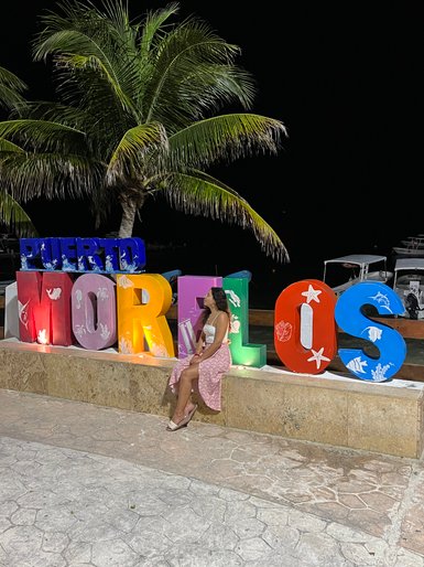 Mädchen sitzt vor dem farbenfrohen Puerto-Morelos-Schriftzug – Mexiko Familienreise