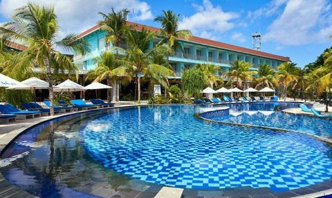 Ein luxuriöser Pool mit blauen Fliesen, umgeben von Palmen und Liegen, unter einem strahlend blauen Himmel.