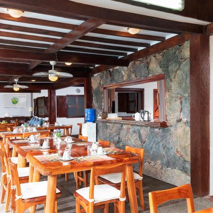 Ein einladender Essbereich mit Holztischen und Stühlen, umgeben von einer rustikalen Steinwand und offenen Fenstern.