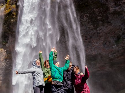 Sechs fröhliche Menschen springen vor dem beeindruckenden Seljalandsfoss-Wasserfall in Island in die Luft.