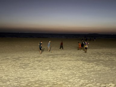 Am Strand spielen mehrere Kinder Fußball, während die Dämmerung über dem Meer leuchtet und die Wellen sanft plätschern.