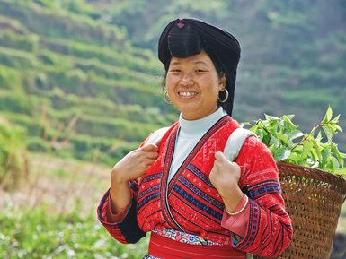 Einheimische Frau der Yao-Minderheit mit traditioneller Kleidung lächelt in die Kamera vor den Reisterrassen von Longsheng – China Familienreise
