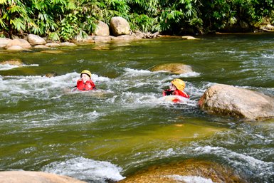Zwei Kinder schwimmen lachend im klaren Flusswasser nach dem Rafting-Abenteuer – Malaysia & Borneo Familienreise