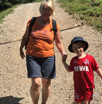 Eine fröhliche Großmutter und ihr Enkelkind spazieren Hand in Hand auf einem sonnigen Wanderweg durch die Natur.