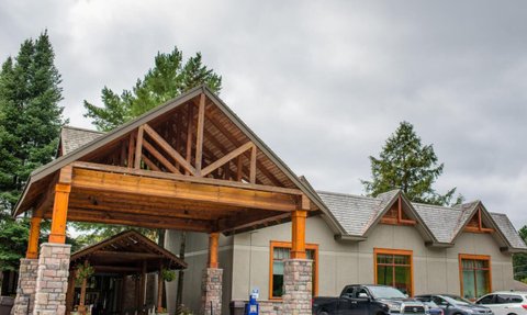 Die Außenansicht eines Resorts mit einem großen Holzvordach und modernen Fenstern, umgeben von Bäumen und Autos.