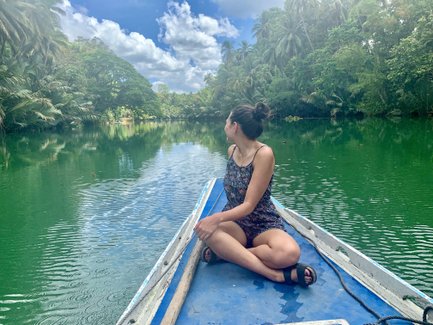 Eine Frau sitzt auf einem Boot und blickt auf den ruhigen, grünen Loboc-Fluss, umgeben von üppiger Vegetation.
