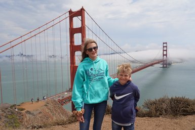 Zwei Kinder stehen lächelnd vor der Golden Gate Bridge, die majestätisch im Hintergrund über das Wasser ragt.