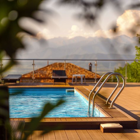 Ein glitzernder Pool mit einer eleganten Treppe, umgeben von einer Holzterrasse und Blick auf die Berge im Hintergrund.