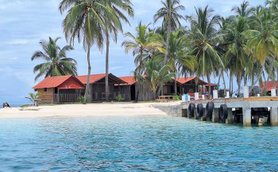 Ein abgelegener Strand mit einer Reihe von traditionellen Hütten unter hohen Palmen, untermalt von sanften Wellen des turquoise Wassers.