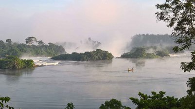 Ein ruhiger Fluss schlängelt sich durch eine grüne Landschaft, während Nebel über den Wasseroberfläche schwebt.