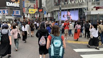 Eine belebte Straße in Shibuya, Tokio, mit vielen Fußgängern und einem großen Starbucks-Schild im Hintergrund.