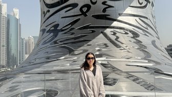 Eine Frau steht auf einer modernen Plattform mit reflektierender Oberfläche, umgeben von futuristischer Architektur und Wolkenkratzern.